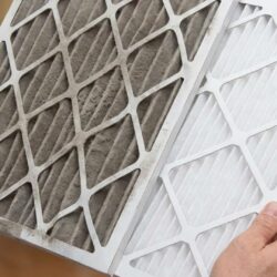 A person's hands hold up a clogged, gray furnace filter beside a new, white replacement filter.