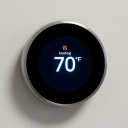 A close-up shot of a modern, round smart thermostat with a digital interface showing 70 degrees.