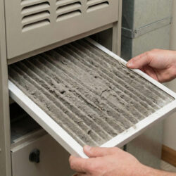 Hands pulling a severely clogged, dirty air filter from a furnace slot.